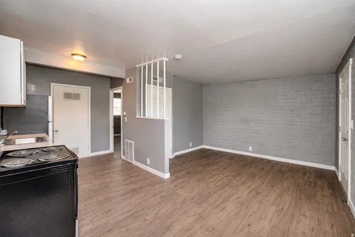 Kitchen with black range with electric cooktop, dark wood finished floors, freestanding refrigerator, brick wall, and light countertops