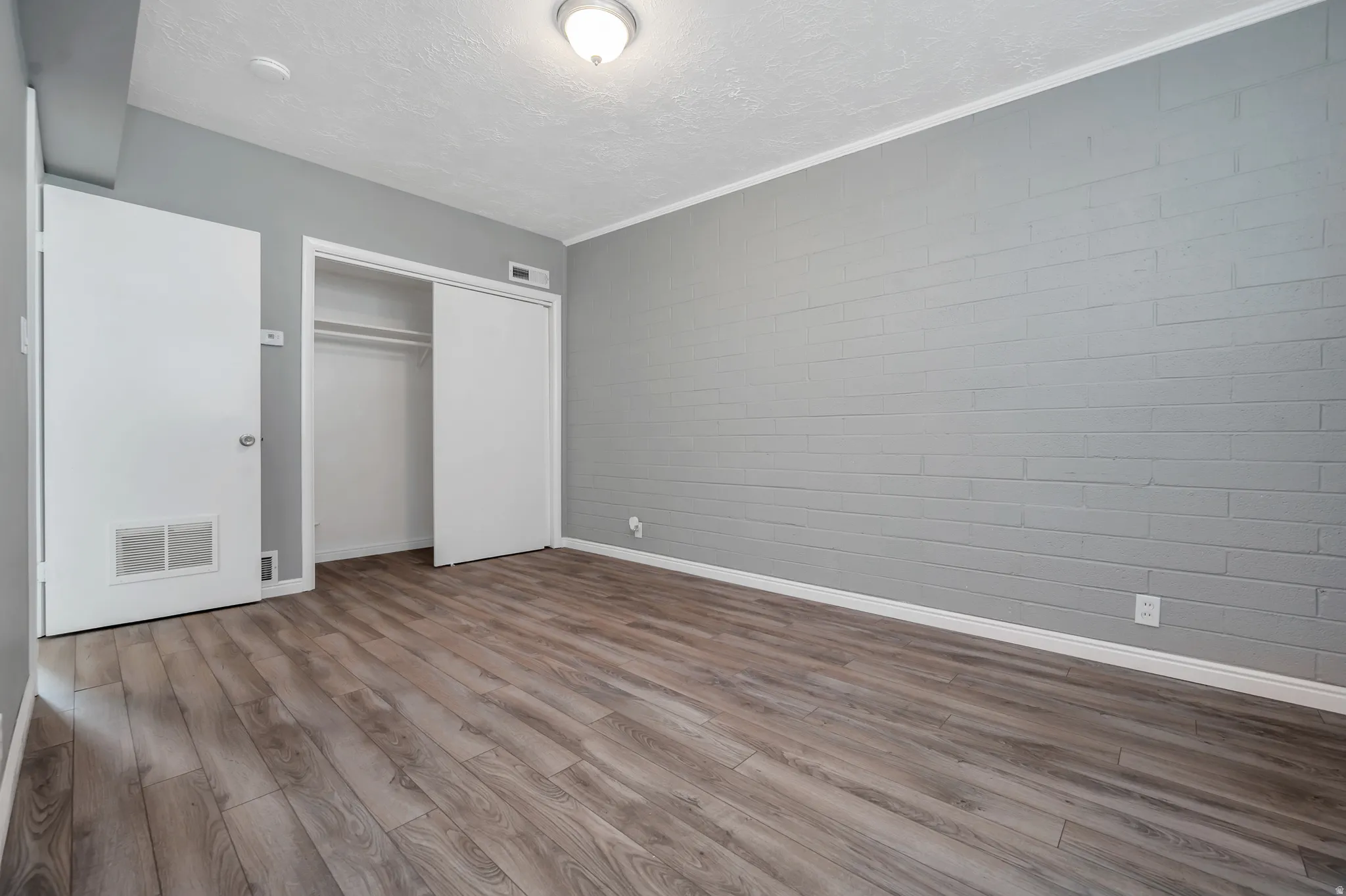 Unfurnished bedroom with a closet, wood finished floors, a textured ceiling, and concrete block wall