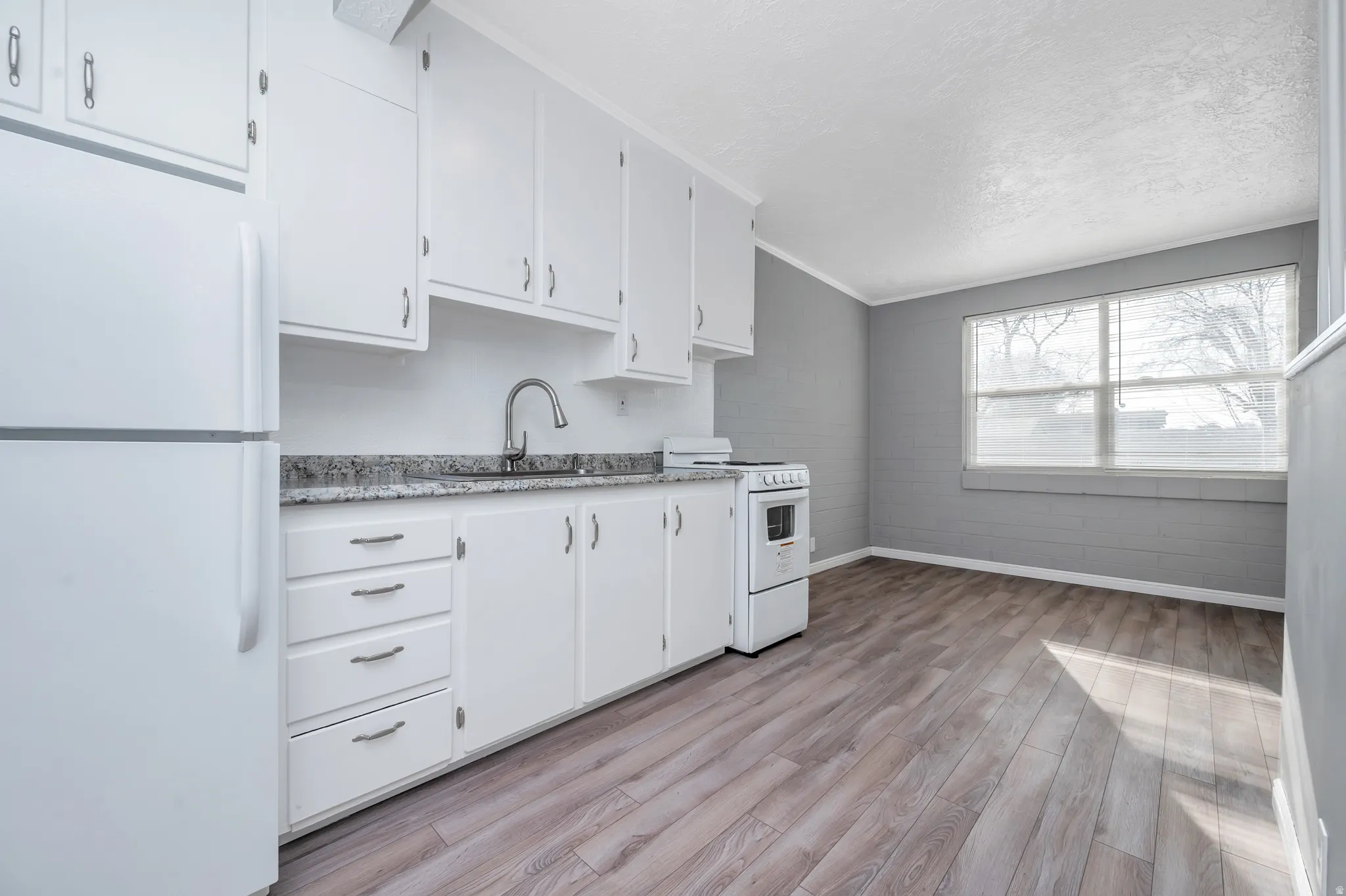 Kitchen featuring white appliances, white cabinets, light wood-style floors, ornamental molding, and a textured ceiling