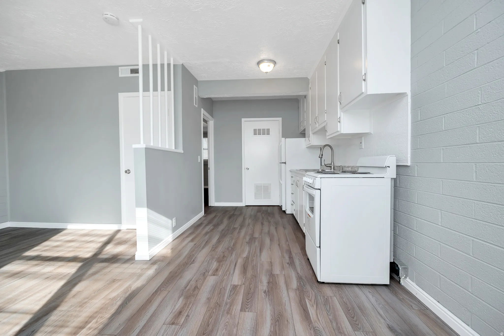 Kitchen featuring white stove, light countertops, white cabinetry, light wood finished floors, and a textured ceiling