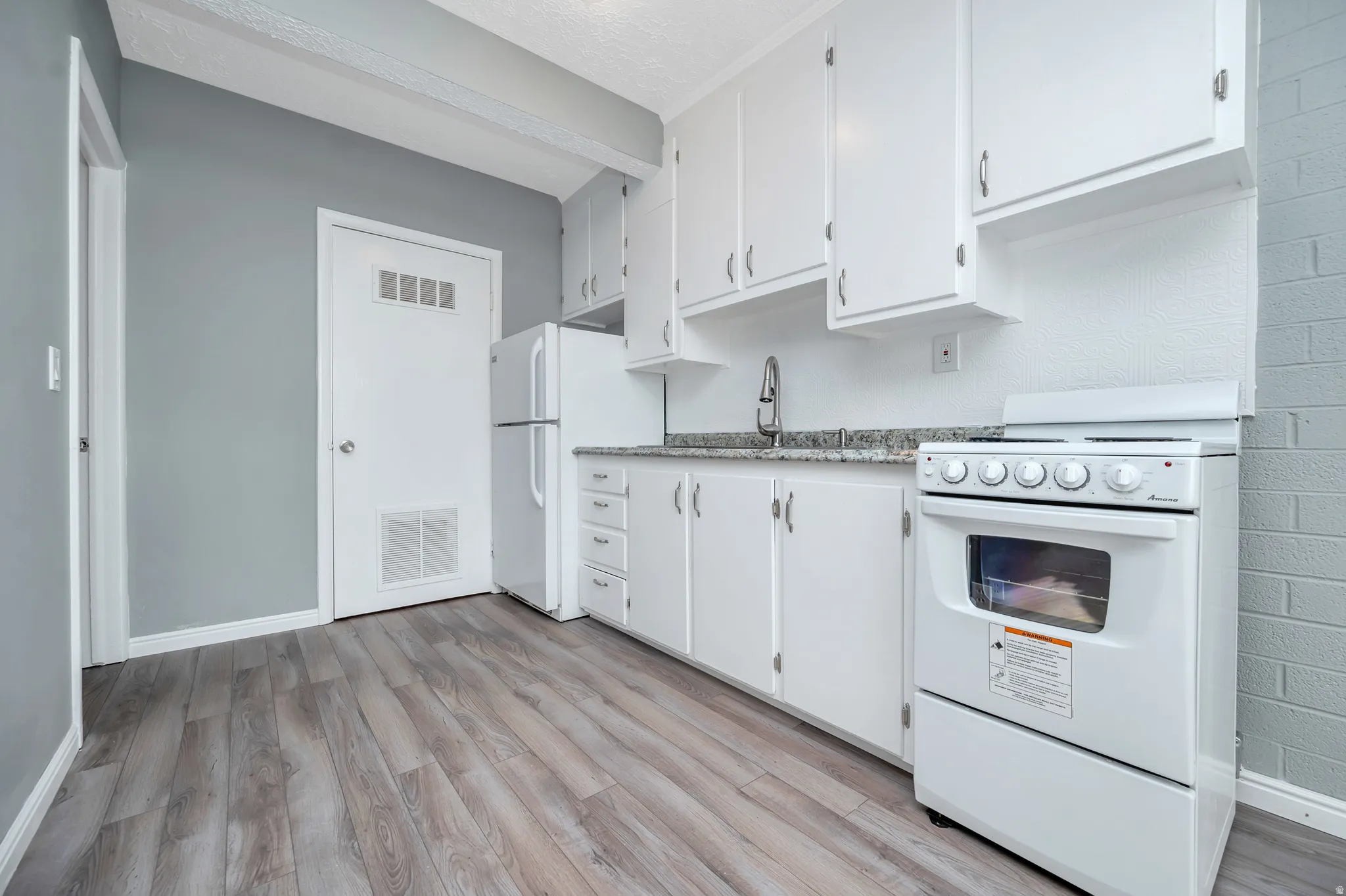 Kitchen with white appliances, white cabinets, light wood finished floors, and light stone countertops