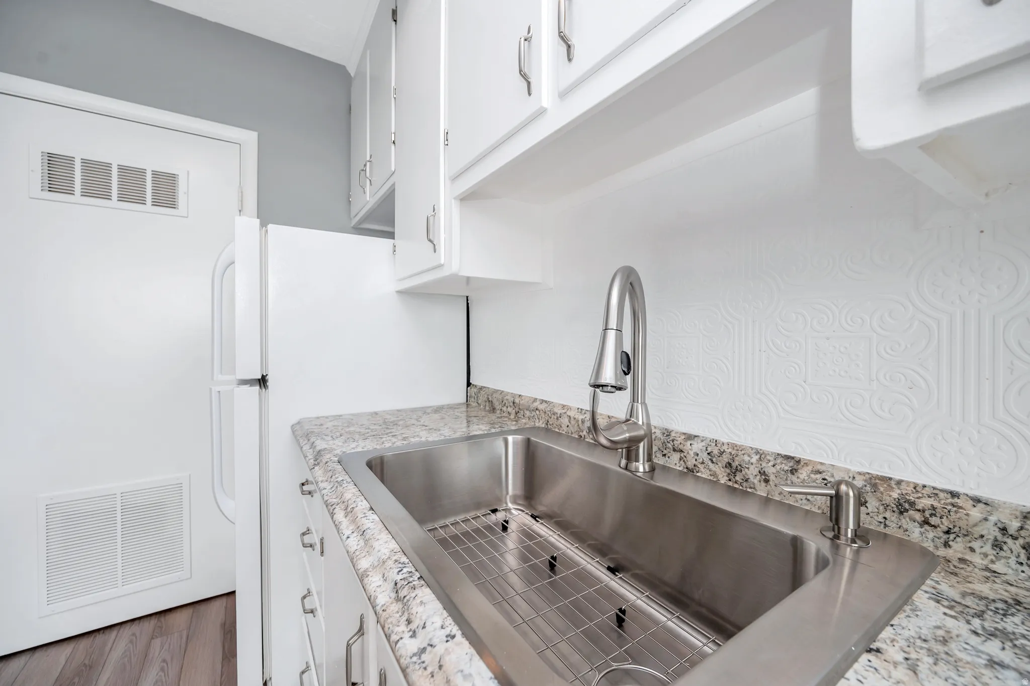 Kitchen with white cabinetry, freestanding refrigerator, light stone countertops, and wood finished floors