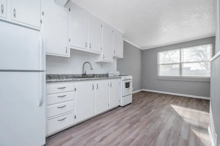 Kitchen featuring white appliances, white cabinets, light wood-style floors, ornamental molding, and a textured ceiling