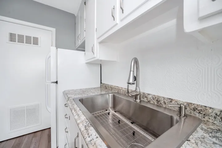 Kitchen with white cabinetry, freestanding refrigerator, light stone countertops, and wood finished floors