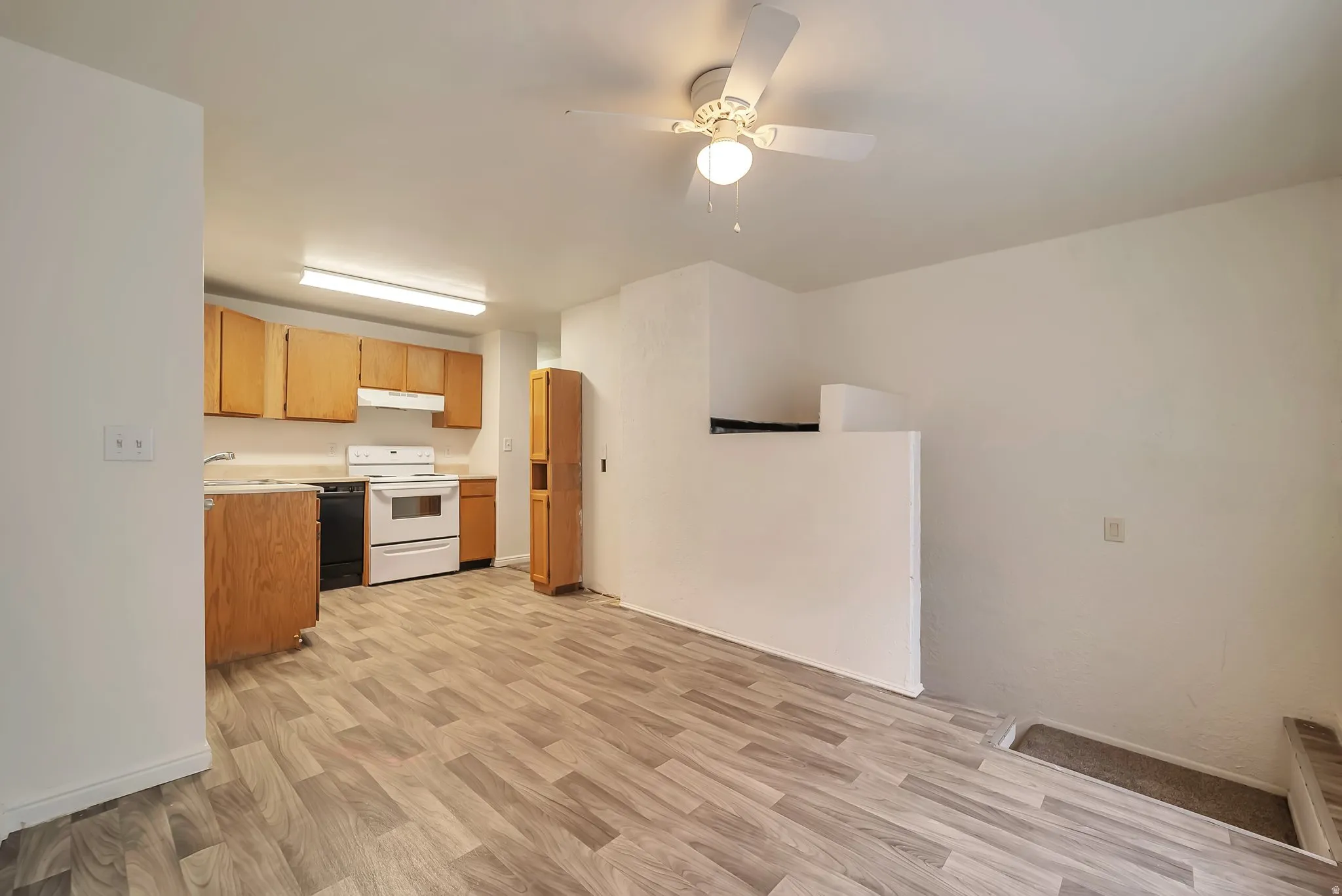 Open-concept kitchen and living area featuring wood-finish flooring, white walls, and a ceiling fan with integrated lighting