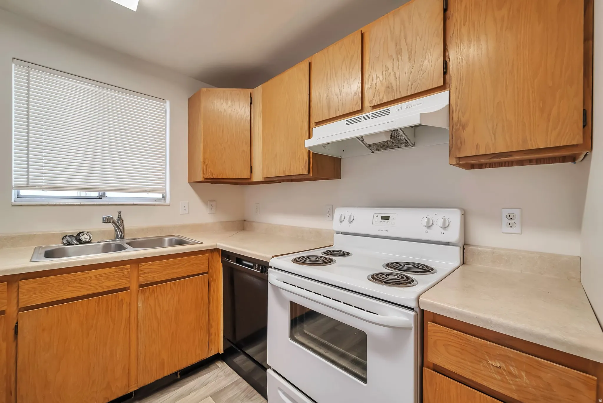 Kitchen featuring wood cabinetry, light-toned countertops, a stainless steel double sink with a chrome faucet, and a white electric range with an overhead hood