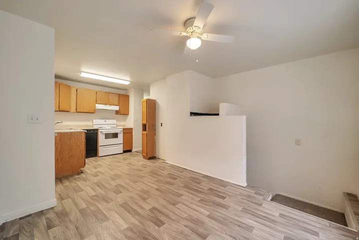 Open-concept kitchen and living area featuring wood-finish flooring, white walls, and a ceiling fan with integrated lighting