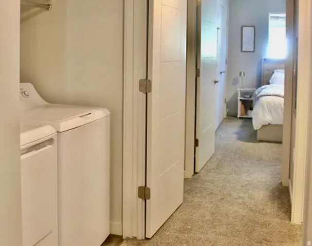 Convenient laundry area featuring a white top-load washer and dryer set, adjacent to a hallway with neutral carpeting