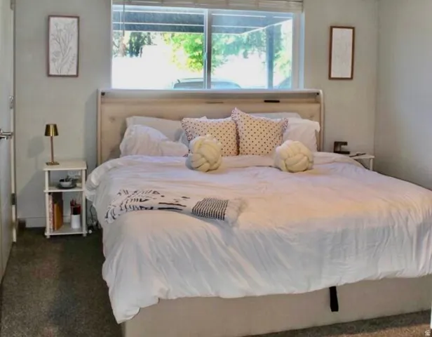 Window-framed sleeping area featuring wall-to-wall carpeting and neutral wall tones