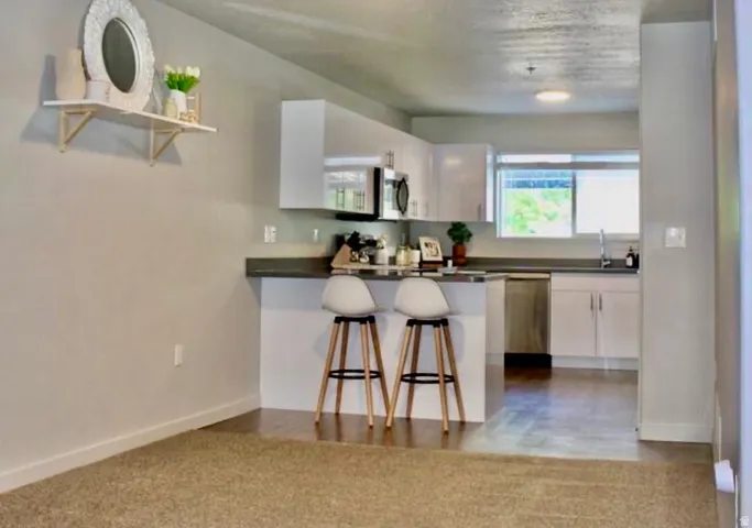 Open-concept kitchen featuring white cabinetry, stainless steel appliances, a breakfast bar, and wood-finish flooring