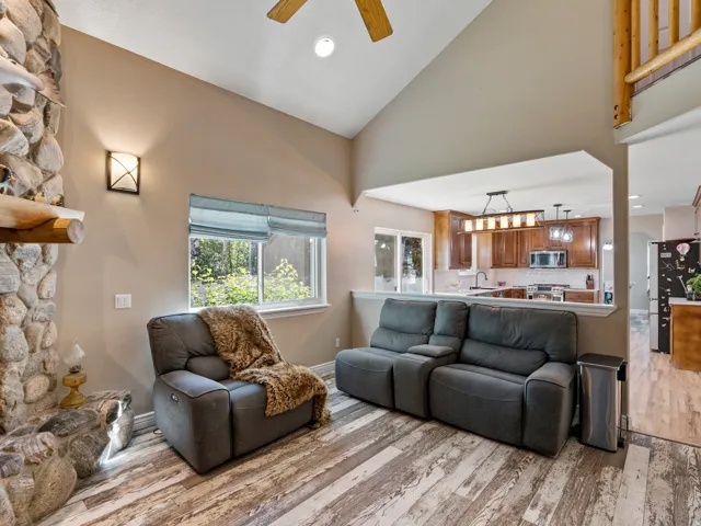 Living area featuring vaulted ceilings with a ceiling fan, stone-clad fireplace, and wood-finish flooring