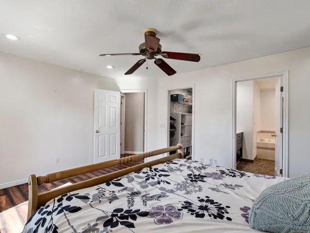 Bedroom featuring recessed lighting, a ceiling fan, wood-finish flooring, and two paneled doors providing access to a closet with built-in shelving and a separate bathroom with tiled flooring