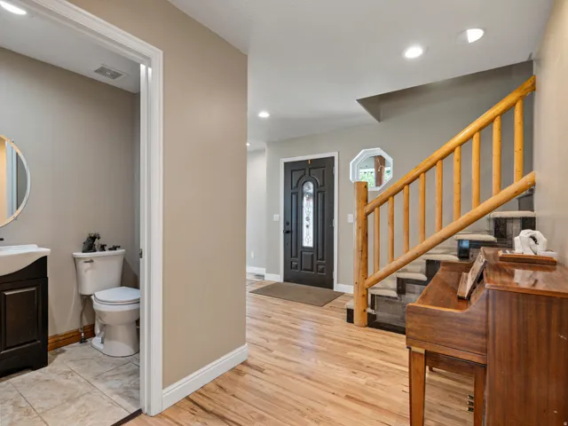 Entryway featuring wood-finish flooring, a dark entry door with decorative glass, recessed lighting, and a prominent staircase with log-style railings