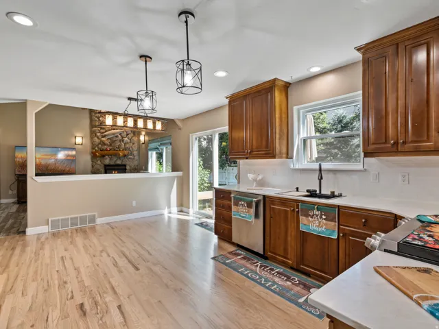 Open-concept kitchen and dining area featuring light wood-finish flooring, a kitchen with wood cabinetry and light countertops, a white subway tile backsplash, and a sliding glass door providing outdoor access
