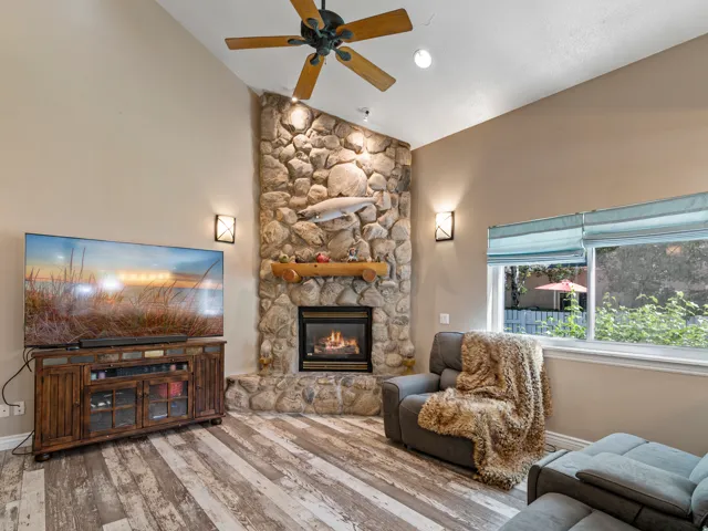 Vaulted ceiling living area featuring a stone-faced fireplace with a wood mantel, gas insert, and wall sconces