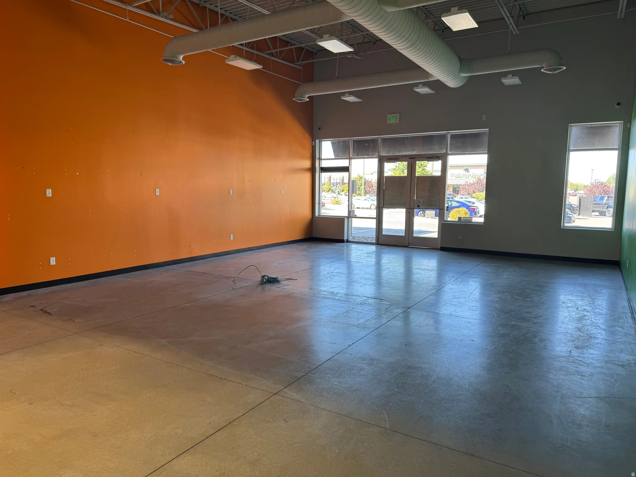 Spacious open-concept interior featuring concrete flooring, exposed ceiling ductwork, and abundant natural light through multiple windows and a glass entry