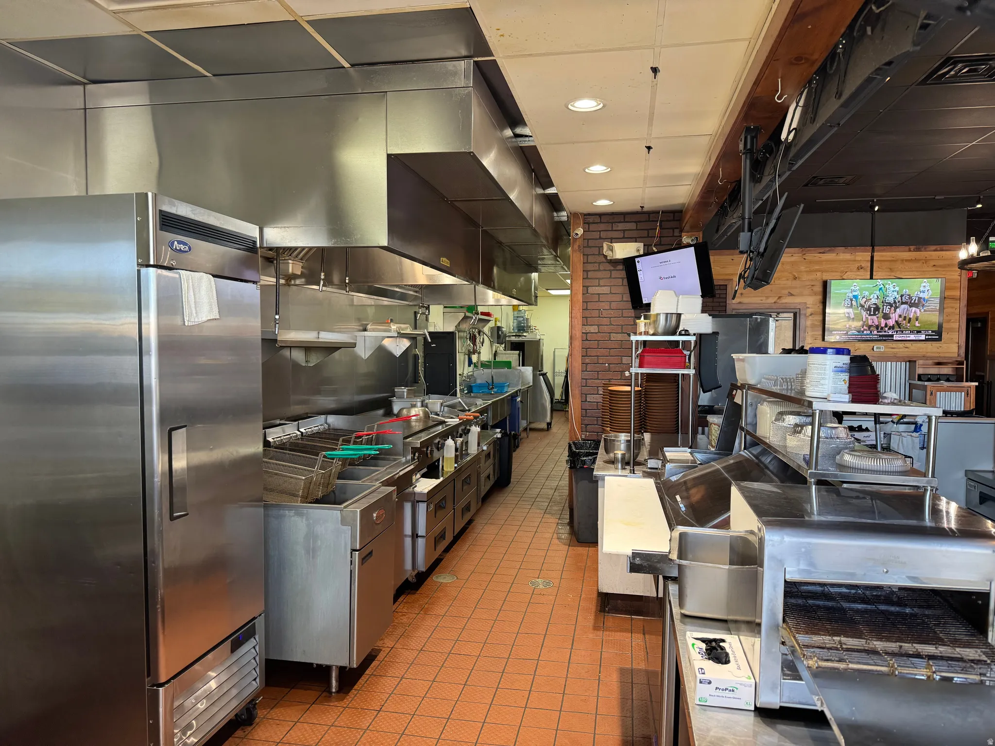 Commercial kitchen space featuring stainless steel appliances, extensive ventilation hood system, and durable tile flooring