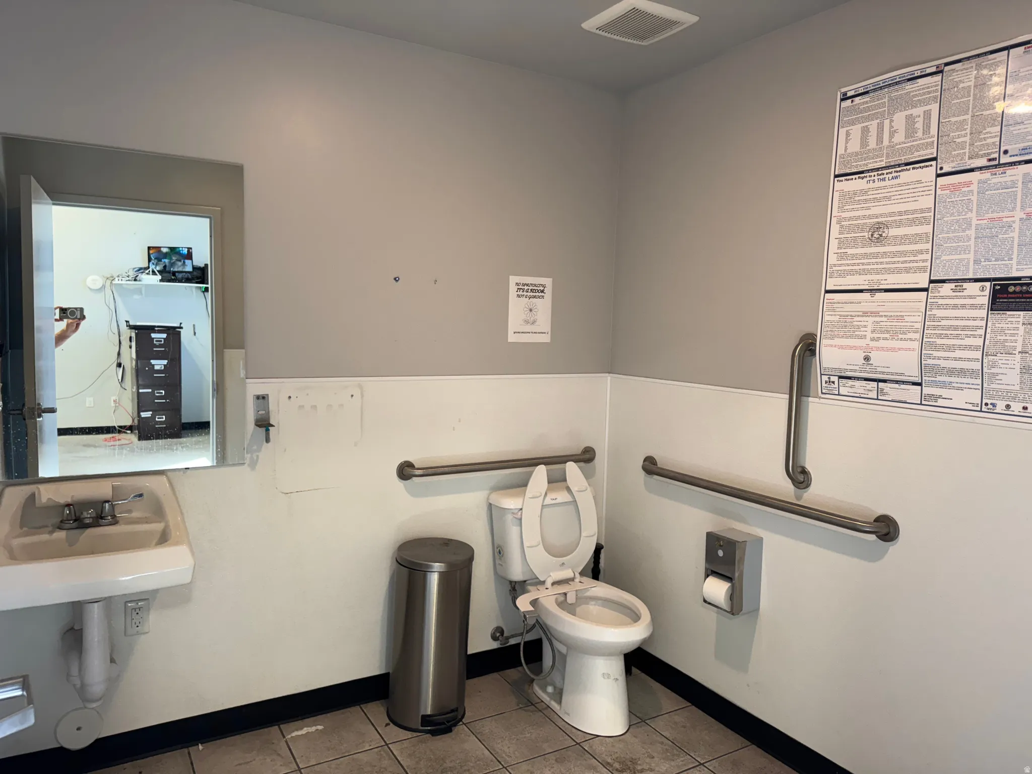 Restroom featuring a wall-mounted sink, toilet with grab bars, and tiled flooring