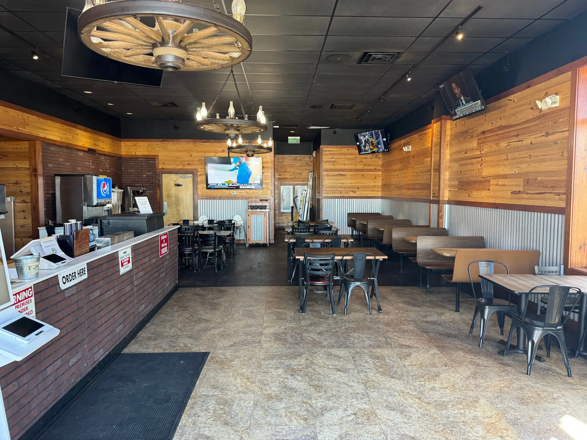 Spacious commercial interior featuring wood paneling, corrugated metal wainscoting, a brick-faced service counter, and wagon wheel light fixtures