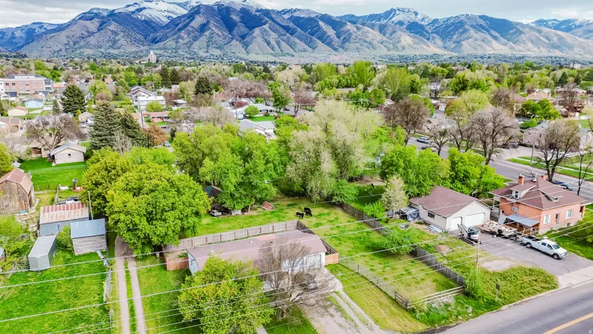 Expansive property featuring multiple structures, mature trees, open green spaces, and a mountainous backdrop