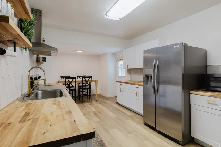 Modern kitchen featuring butcher block countertops, stainless steel appliances, white cabinetry with gold-tone hardware, and a unique geometric tile backsplash