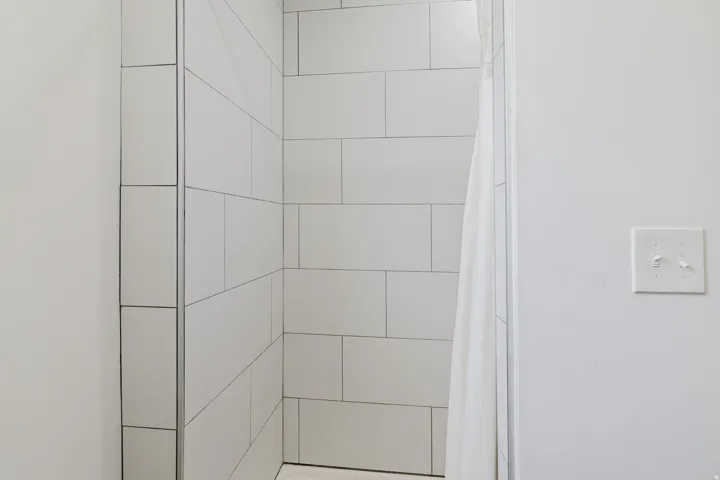 Shower enclosure featuring white subway tile with dark grout