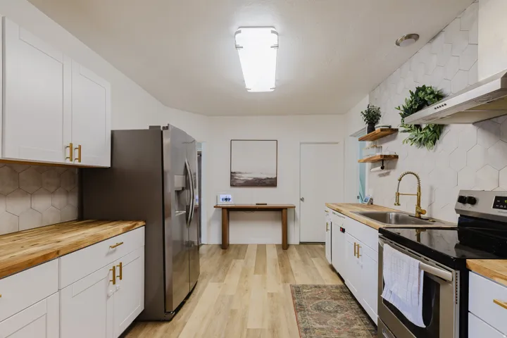 Modern kitchen featuring white shaker cabinetry, wood-finish countertops, stainless steel appliances, a hexagonal tile backsplash, and light wood-finish flooring
