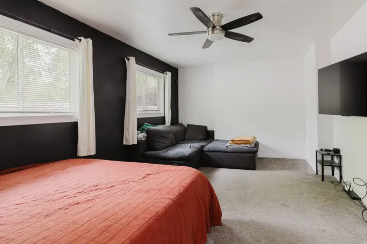 Carpeted room featuring a ceiling fan with integrated lighting, two windows with blinds, and white trim