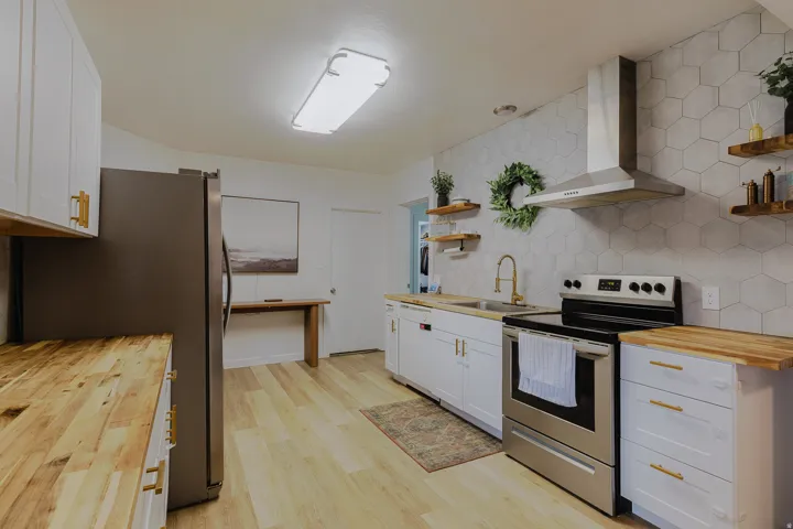 Contemporary kitchen featuring light wood-finish flooring, white cabinetry with gold-tone hardware, butcher block countertops, a stainless steel range, and a hexagonal tile backsplash