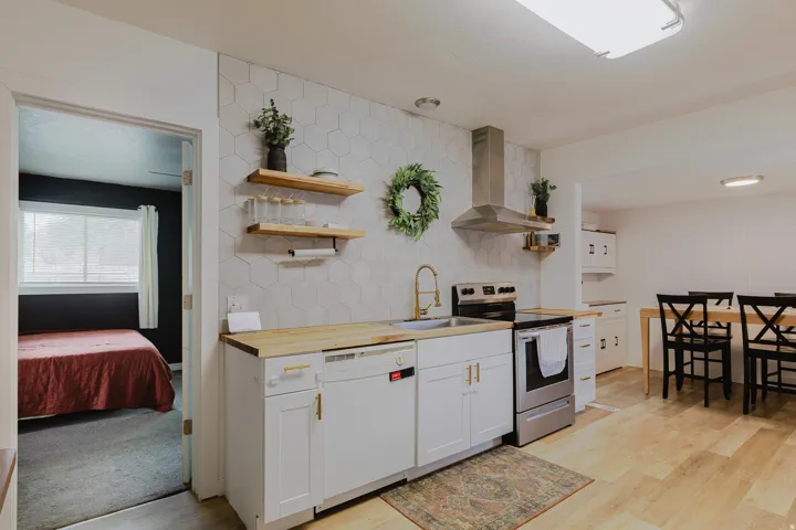 Modern kitchen featuring white cabinetry with gold-tone hardware, wood-finish countertops, a hexagonal tile backsplash, stainless steel appliances, and a gold-tone faucet