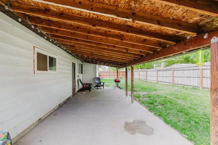 Expansive covered patio featuring a concrete surface, exposed wood beam ceiling, and white siding exterior