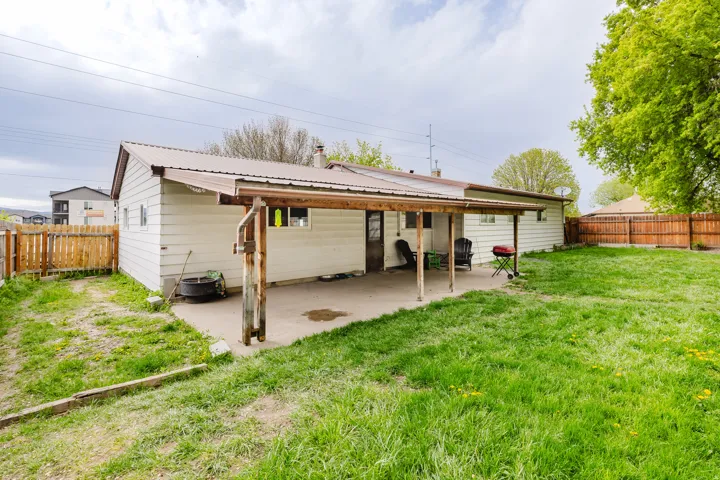 Expansive backyard featuring a concrete patio with a covered overhang, a brown wood privacy fence, and mature perimeter trees