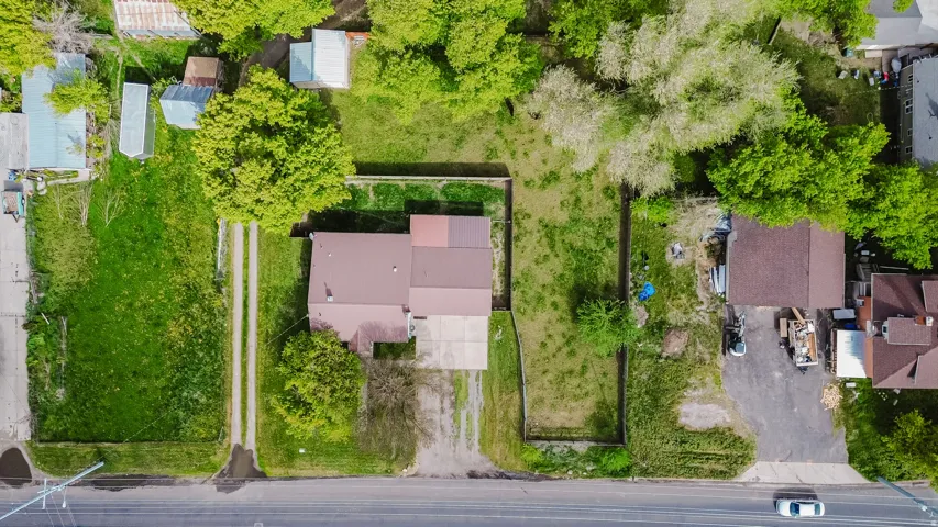 Property featuring a brown-roofed structure, a paved driveway, a gravel access path, and expansive green spaces