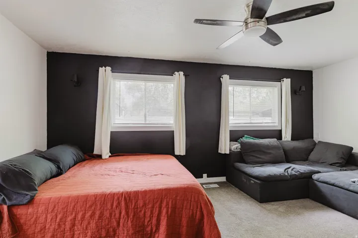 Interior room featuring a bold accent wall, two windows with blinds and curtains, and a ceiling fan