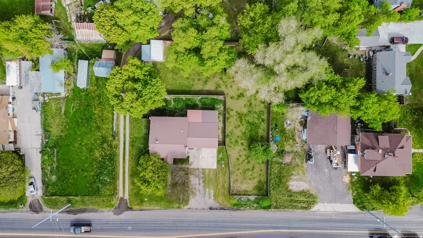 Aerial perspective showcasing a parcel with a brown-roofed structure, featuring a gravel driveway, mature trees, and extensive green space