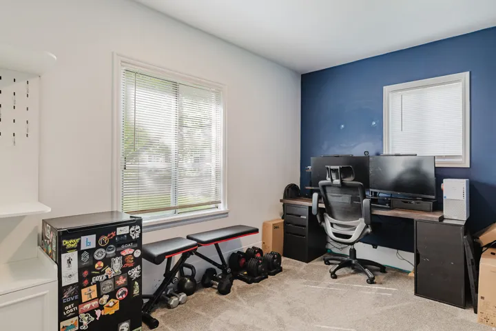 Carpeted room with a dedicated accent wall, featuring a window with horizontal blinds and a built-in shelving unit