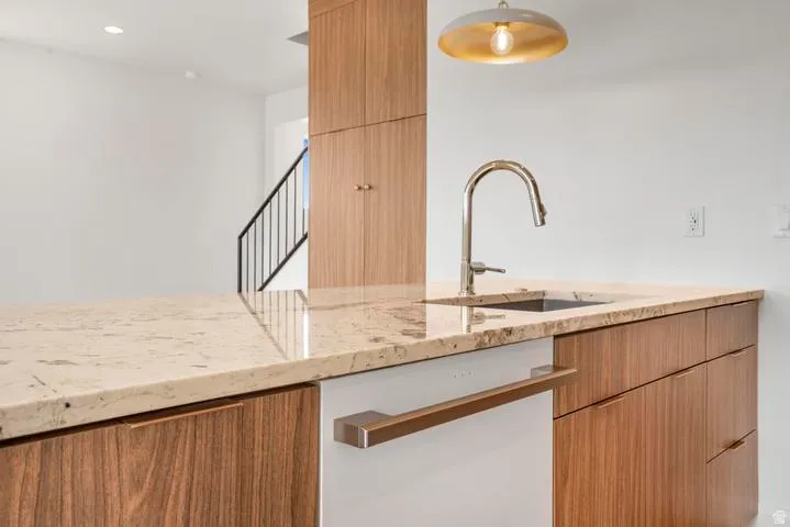 Kitchen island featuring stone countertops, integrated sink with gooseneck faucet, paneled dishwasher, and wood-finish cabinetry