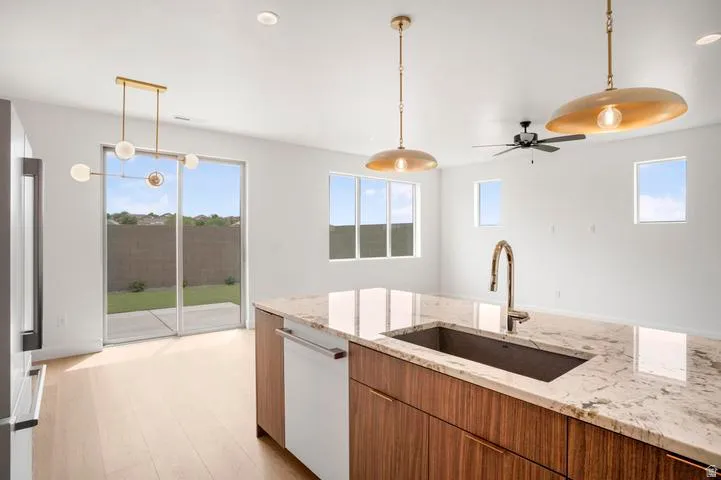 Kitchen island featuring a large undermount sink with a gooseneck faucet, light-toned stone countertop, and wood-finish cabinetry