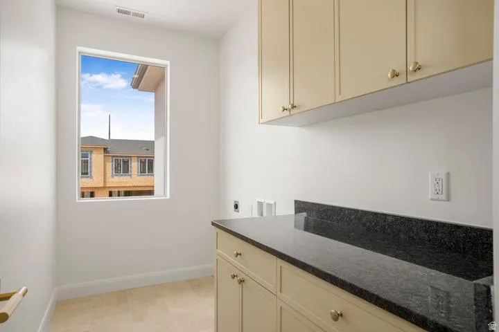 Utility space featuring a single window, upper and lower cabinetry, a dark countertop, and tile flooring