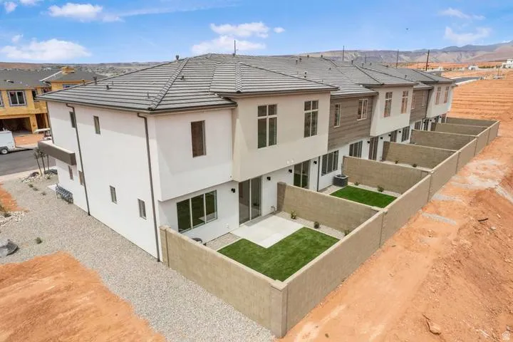 Row of newly constructed townhomes featuring stucco and horizontal siding exteriors, individual private fenced yards with artificial turf and concrete patios, and gravel landscaping