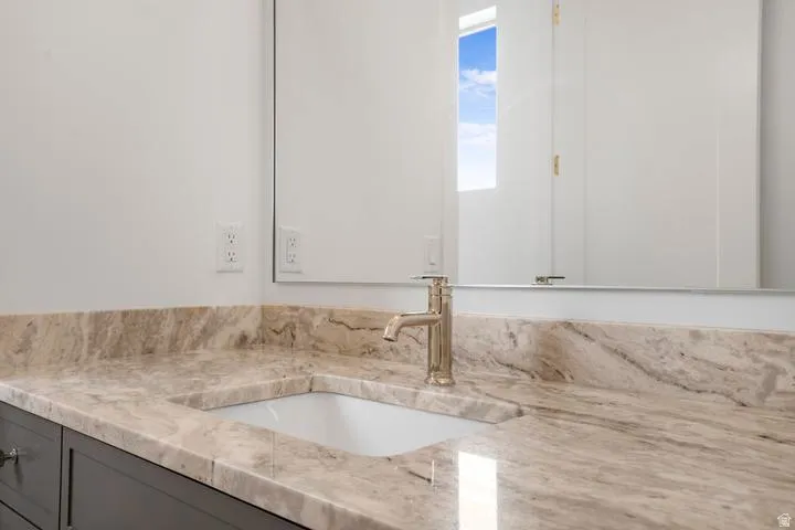 Bathroom vanity featuring a polished stone countertop, integrated rectangular sink, and single-handle faucet