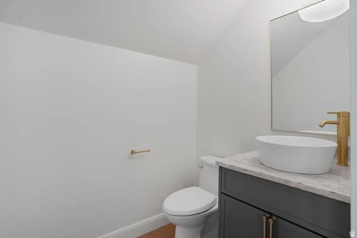 Contemporary powder room featuring a white vessel sink, gold-finish faucet, and a dark gray vanity with a stone countertop