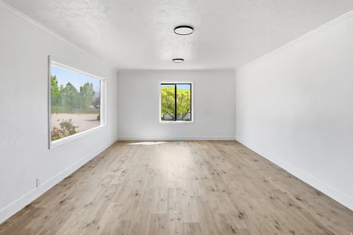 Spacious room featuring wood-finish flooring, white walls, and crown molding