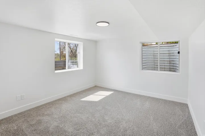 Bright room featuring light gray carpet, white walls, two windows, and a flush-mount ceiling light fixture