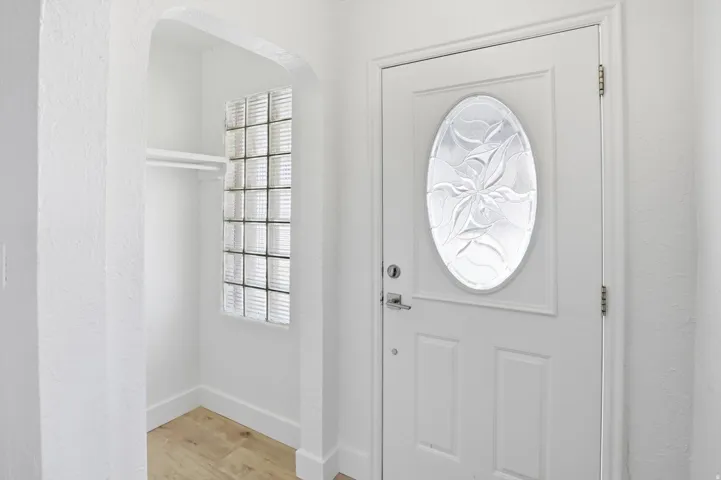Entryway featuring a white paneled door with an oval decorative glass insert, a recessed alcove with a clothing rod and shelf, glass block window, and wood-finish flooring