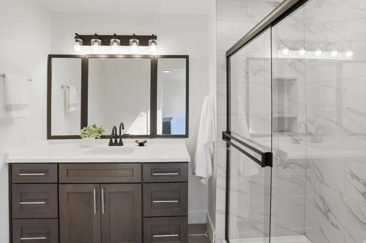 Modern bathroom featuring a dark wood-finish vanity with ample storage, a white countertop, and dual framed mirrors