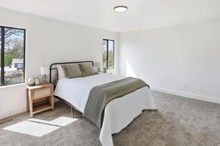 Bedroom featuring two black-framed windows, a flush-mount ceiling light, white walls, and gray carpet flooring