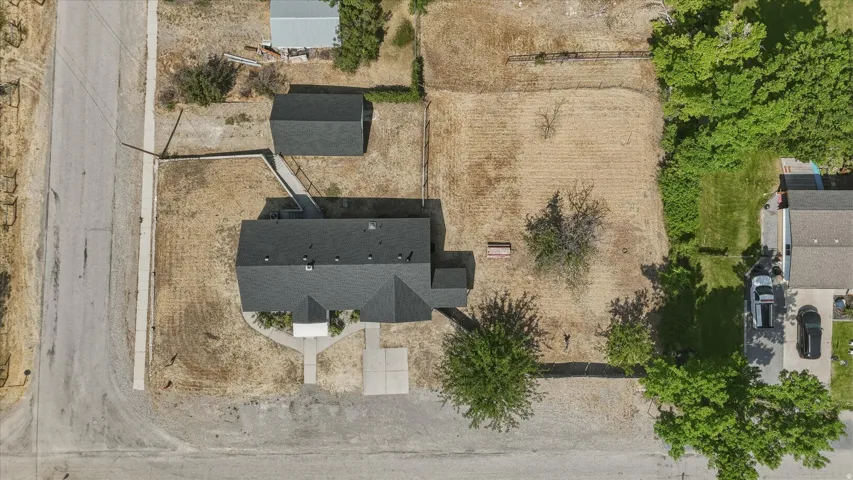 Property featuring a dark shingle roof, a detached shed, a paved driveway, and mature trees