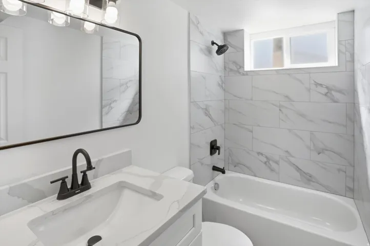 Bathroom featuring a white vanity with quartz-style countertop and integrated sink, a contemporary black-framed mirror, and a modern black faucet
