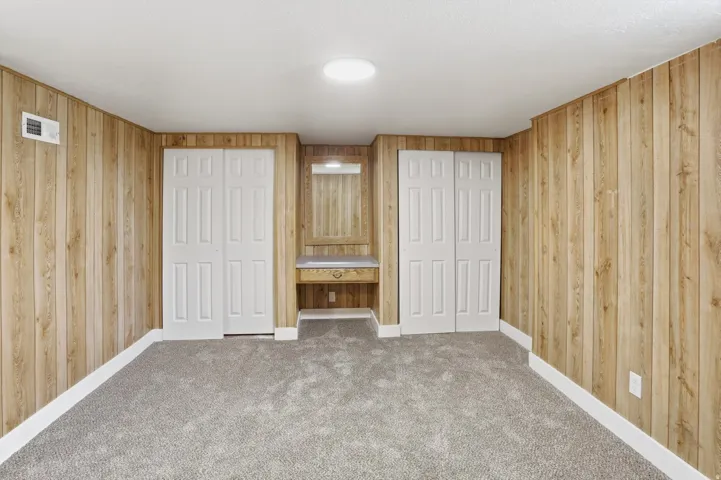 Carpeted room featuring wood-paneled walls, white baseboards, and two bi-fold closet doors